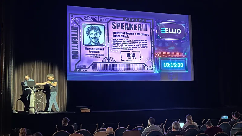 Image shows a stage with large sreen displaying BSIdes Prague graphicsELLIO logo, and Marco Balduzzi from Trend Micro
