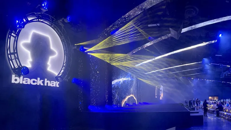 Black Hat cybersecurity conference stage with dramatic blue lighting, featuring the Black Hat logo and geometric light projections over an audience