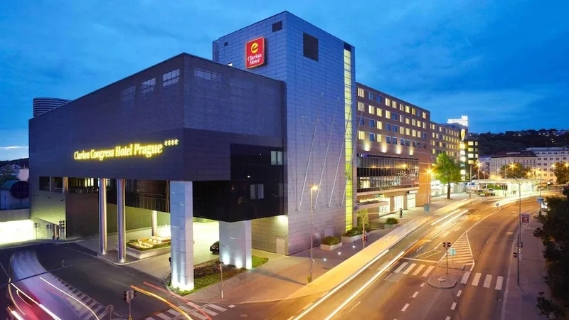 Modern hotel building at dusk with "Clarion Congress Hotel Prague" signage, illuminated windows, and traffic light trails on surrounding streets