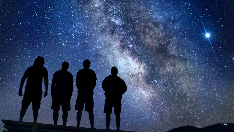 The image shows a group of people gazing at the night sky, where the Milky Way is visible.